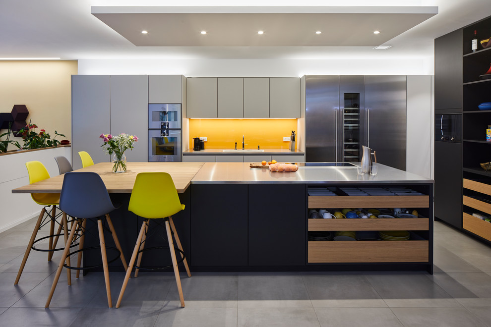 Open concept kitchen - large modern single-wall ceramic tile and gray floor open concept kitchen idea with black cabinets, stainless steel countertops, yellow backsplash, glass sheet backsplash, stainless steel appliances and an island