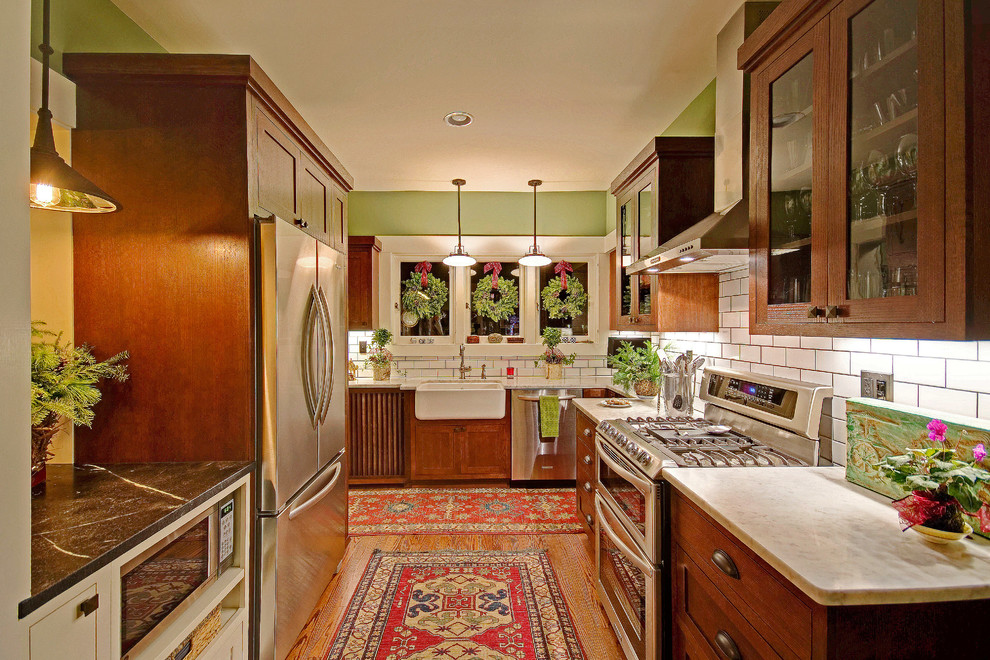 Foto på ett avskilt, mellanstort amerikanskt u-kök, med en rustik diskho, skåp i mellenmörkt trä, marmorbänkskiva, vitt stänkskydd, stänkskydd i tunnelbanekakel, rostfria vitvaror, luckor med profilerade fronter, mellanmörkt trägolv och brunt golv