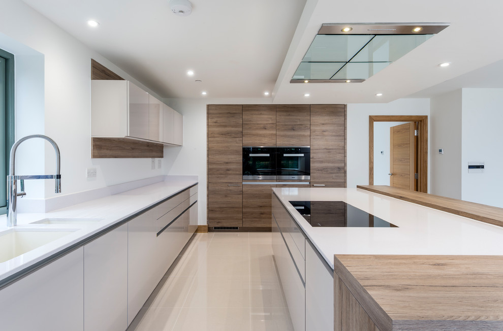 Example of a huge trendy l-shaped porcelain tile and beige floor eat-in kitchen design in Hampshire with an undermount sink, flat-panel cabinets, medium tone wood cabinets, solid surface countertops, black appliances, an island and white countertops