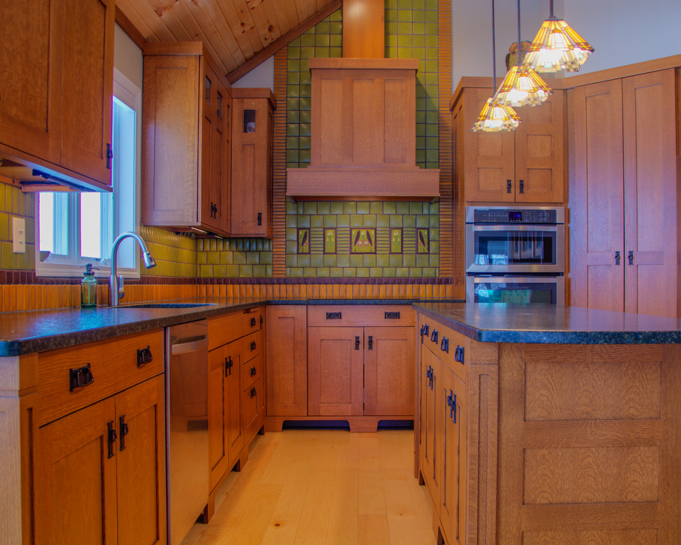 Amerikansk inredning av ett stort l-kök, med en undermonterad diskho, luckor med infälld panel, skåp i mellenmörkt trä, granitbänkskiva, grönt stänkskydd, stänkskydd i keramik, rostfria vitvaror, ljust trägolv och en köksö