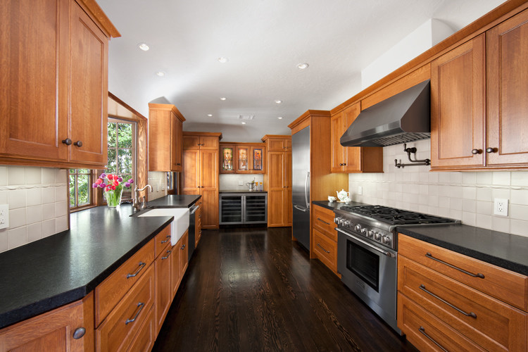 Inspiration for a large traditional galley kitchen pantry in Los Angeles with a belfast sink, recessed-panel cabinets, brown cabinets, composite countertops, beige splashback, ceramic splashback, stainless steel appliances, medium hardwood flooring, no island and brown floors.