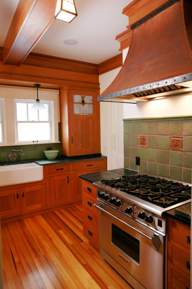 Cette image montre une cuisine américaine craftsman en U et bois brun avec un évier de ferme, un placard à porte shaker, une crédence verte et un électroménager en acier inoxydable.