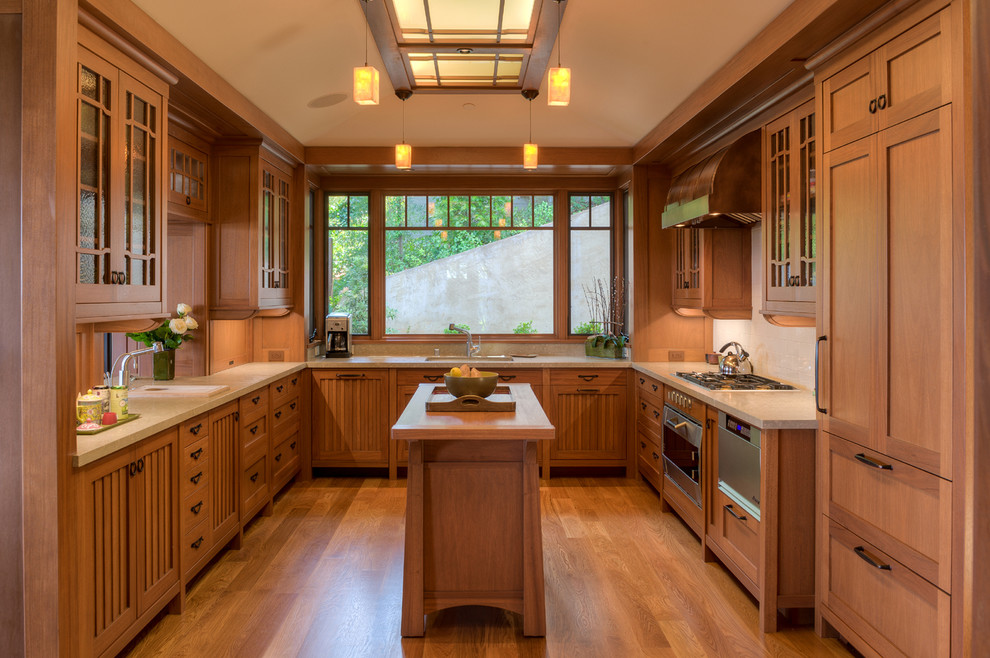 Exemple d'une cuisine encastrable craftsman en U et bois brun avec un placard à porte vitrée, une crédence beige, un sol en bois brun et îlot.
