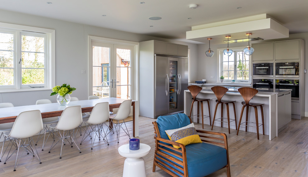 Foto di una cucina contemporanea di medie dimensioni con ante lisce, ante beige, elettrodomestici in acciaio inossidabile, pavimento in legno massello medio, pavimento marrone e top bianco