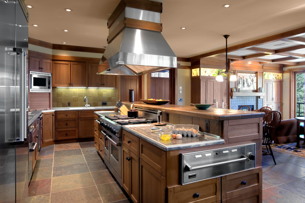 Example of a large arts and crafts l-shaped slate floor and multicolored floor open concept kitchen design in Sacramento with shaker cabinets, medium tone wood cabinets, stainless steel countertops, beige backsplash, travertine backsplash, stainless steel appliances and an island