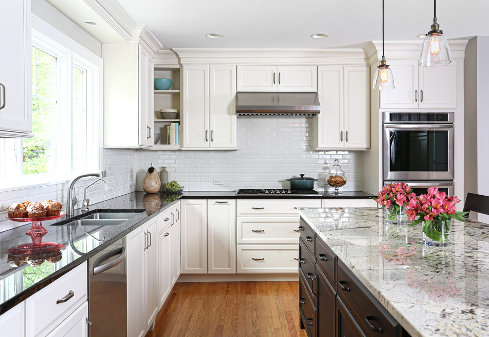 Mid-sized arts and crafts l-shaped light wood floor eat-in kitchen photo in Chicago with an undermount sink, white cabinets, granite countertops, white backsplash, subway tile backsplash, stainless steel appliances and an island