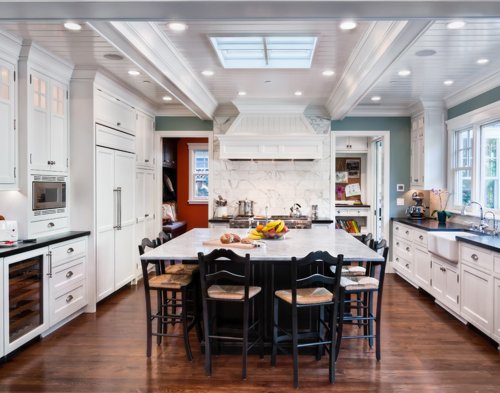 Enclosed kitchen - mid-sized traditional u-shaped dark wood floor enclosed kitchen idea in San Francisco with a farmhouse sink, shaker cabinets, white cabinets, solid surface countertops, white backsplash, stone tile backsplash, stainless steel appliances and an island