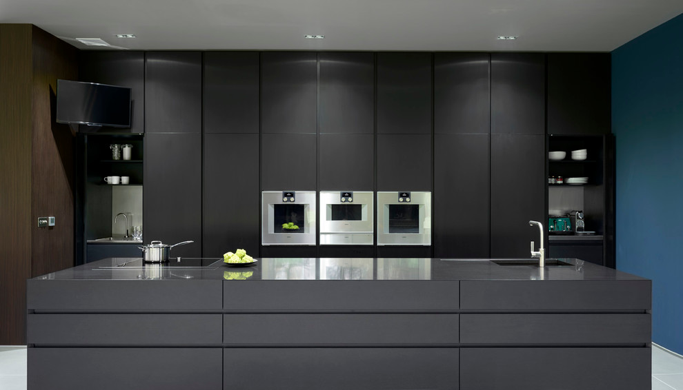 Trendy single-wall open concept kitchen photo in London with an integrated sink, flat-panel cabinets, paneled appliances, an island, black cabinets and granite countertops
