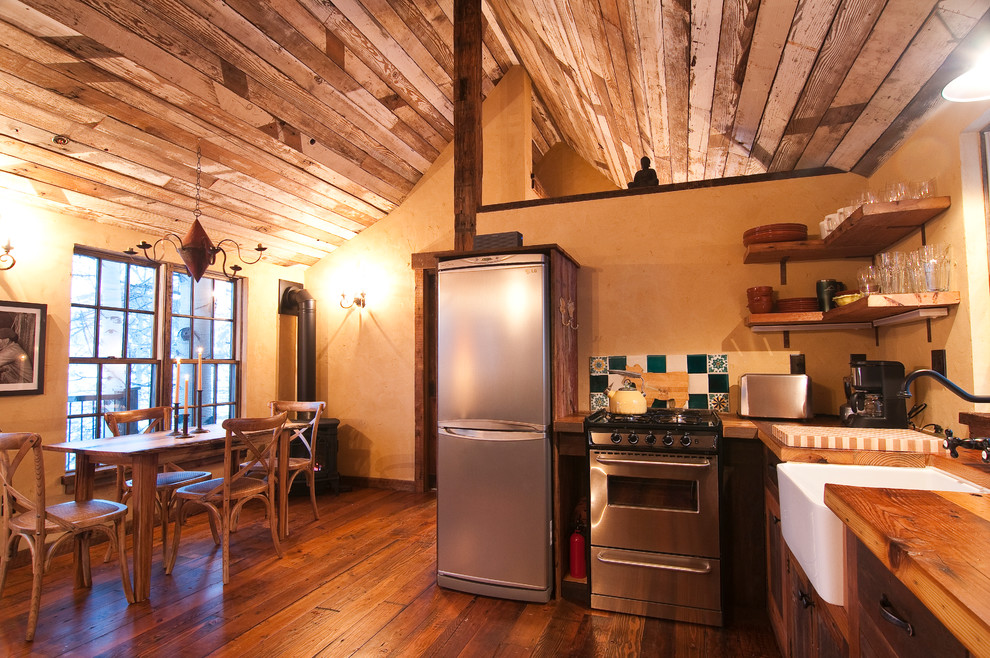 Inredning av ett rustikt litet l-kök, med en rustik diskho, luckor med infälld panel, skåp i mellenmörkt trä, träbänkskiva, rostfria vitvaror och mellanmörkt trägolv