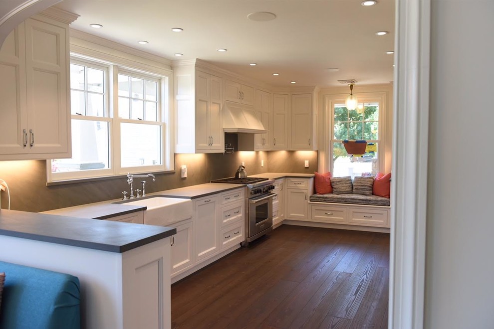 Inspiration for a large coastal l-shaped dark wood floor and brown floor enclosed kitchen remodel in New York with a farmhouse sink, recessed-panel cabinets, white cabinets, concrete countertops, gray backsplash, stone slab backsplash, stainless steel appliances, a peninsula and gray countertops