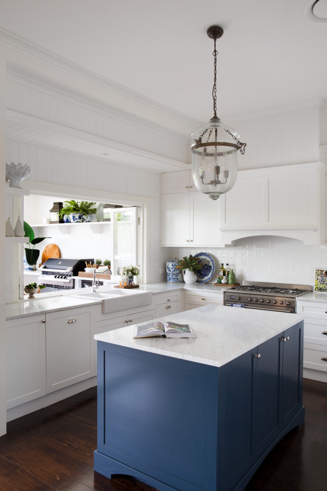 Klassisk inredning av ett stort vit vitt l-kök, med en rustik diskho, skåp i shakerstil, vita skåp, vitt stänkskydd, rostfria vitvaror, mellanmörkt trägolv, en köksö och brunt golv