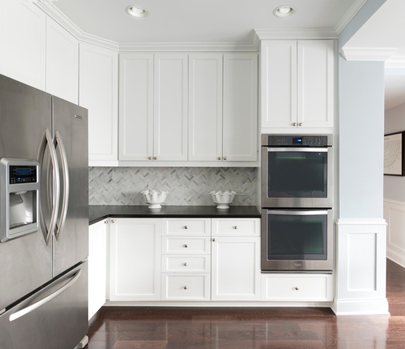 Klassisk inredning av ett mellanstort svart svart kök, med en undermonterad diskho, luckor med infälld panel, vita skåp, bänkskiva i kvarts, vitt stänkskydd, stänkskydd i marmor, rostfria vitvaror, mörkt trägolv, en halv köksö och brunt golv