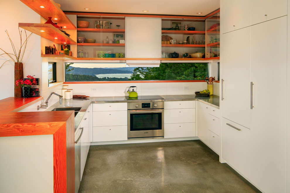 Exempel på ett mellanstort modernt kök, med släta luckor, vita skåp, vitt stänkskydd, betonggolv, en undermonterad diskho, träbänkskiva, vita vitvaror och en halv köksö