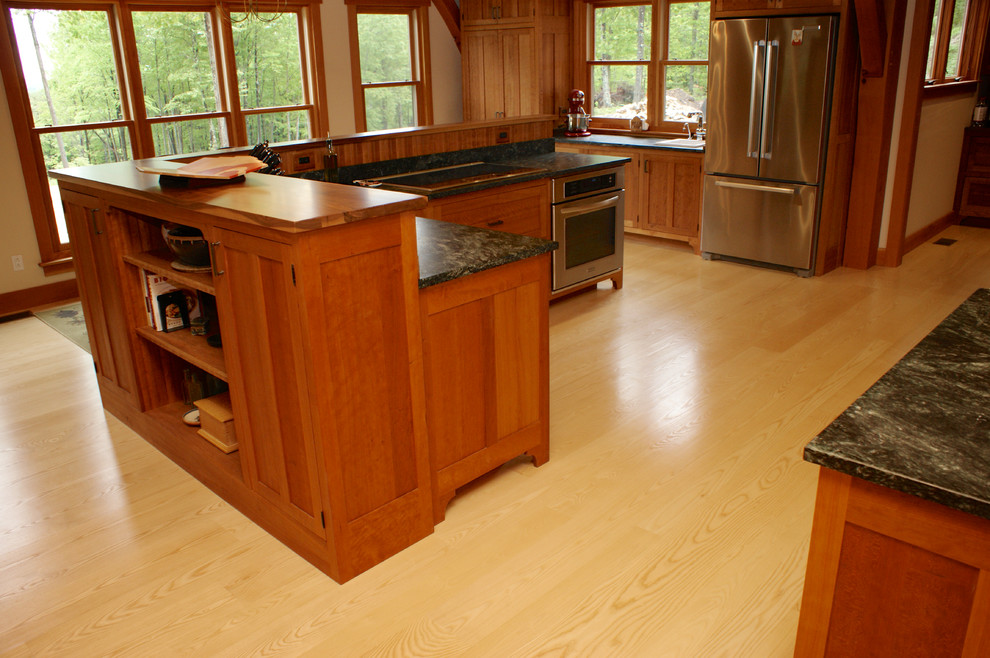 Amerikansk inredning av ett stort l-kök, med ljust trägolv, en nedsänkt diskho, luckor med profilerade fronter, skåp i mellenmörkt trä, rostfria vitvaror och en köksö