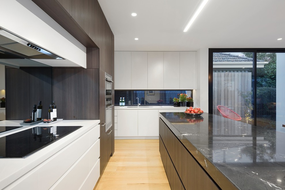 Large modern single-wall open plan kitchen in Melbourne with a submerged sink, white cabinets, engineered stone countertops, multi-coloured splashback, glass sheet splashback, stainless steel appliances, medium hardwood flooring, an island and brown floors.