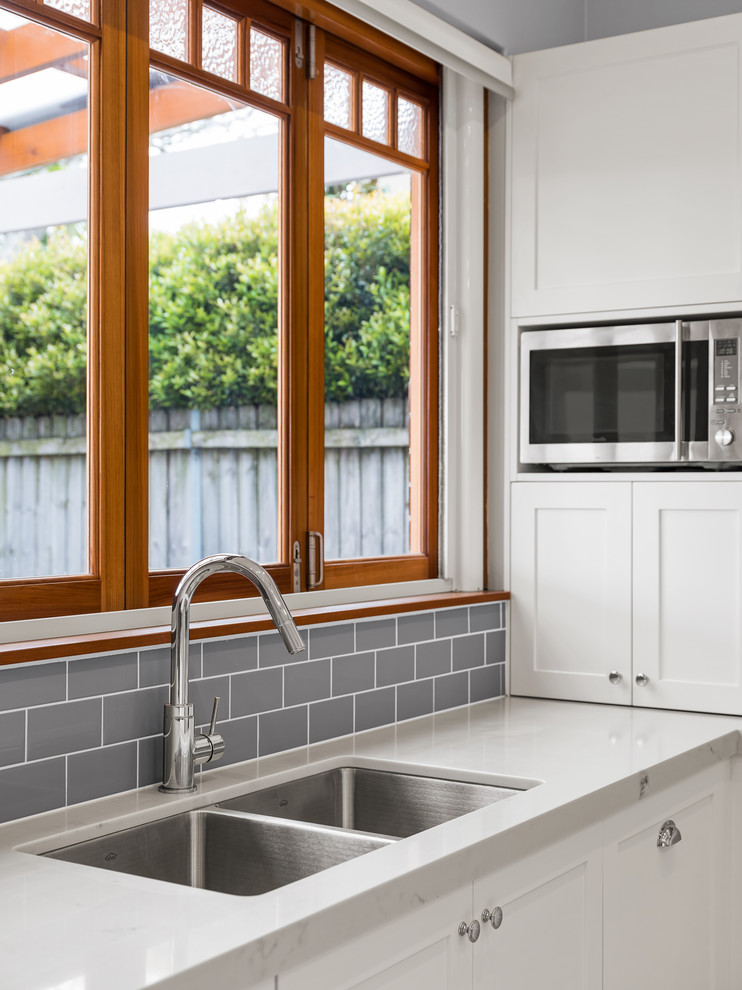 Inspiration for a medium sized classic u-shaped open plan kitchen in Sydney with a submerged sink, shaker cabinets, white cabinets, engineered stone countertops, grey splashback, ceramic splashback, stainless steel appliances, light hardwood flooring, an island, brown floors and grey worktops.