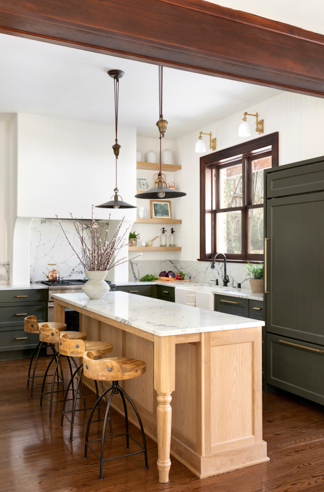 Inredning av ett klassiskt vit vitt l-kök, med en rustik diskho, luckor med infälld panel, gröna skåp, vitt stänkskydd, stänkskydd i sten, integrerade vitvaror, mörkt trägolv, en köksö och brunt golv