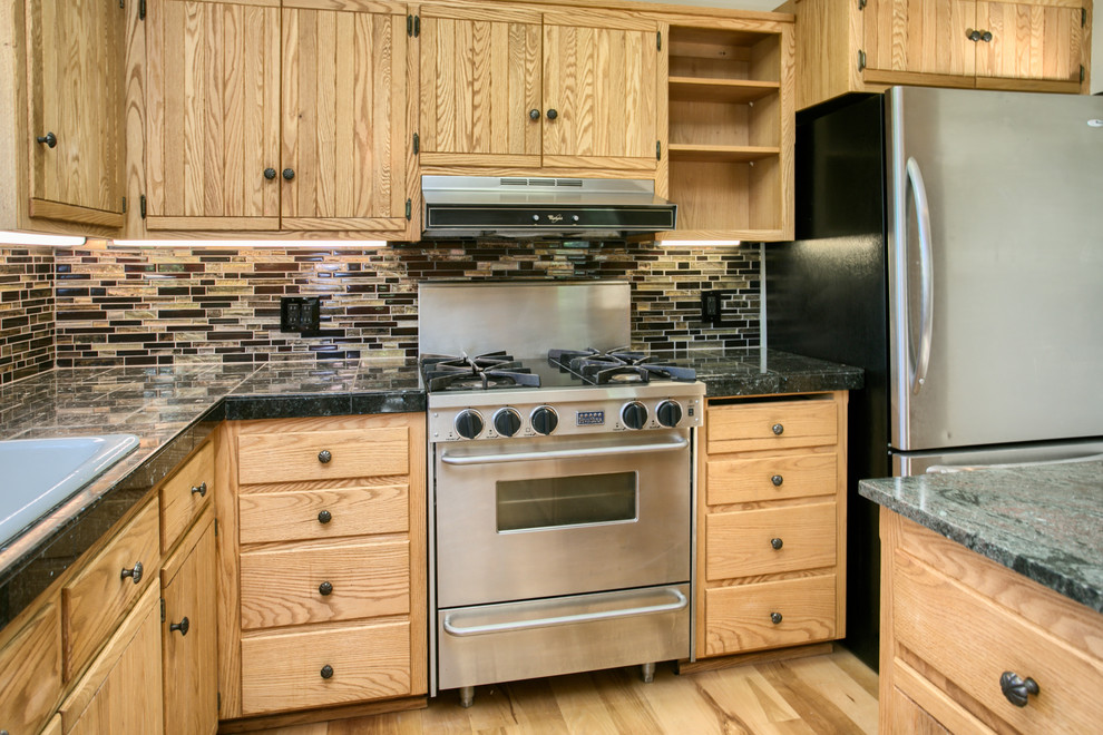 Bild på ett mellanstort amerikanskt l-kök, med en nedsänkt diskho, skåp i shakerstil, skåp i ljust trä, granitbänkskiva, brunt stänkskydd, stänkskydd i stickkakel, rostfria vitvaror, ljust trägolv, en köksö och brunt golv