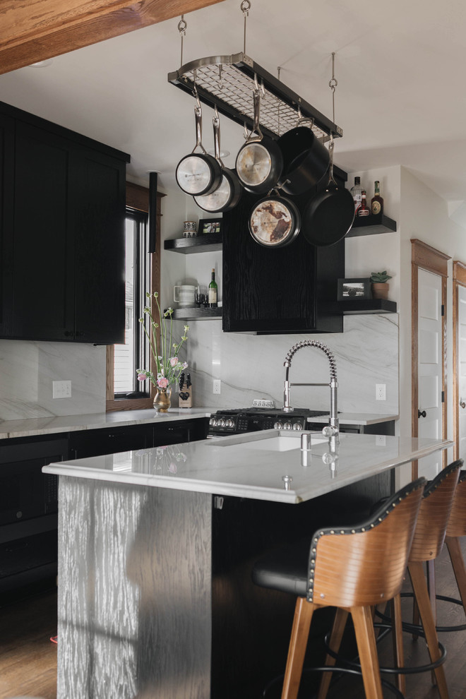 Inredning av ett klassiskt vit vitt kök, med en undermonterad diskho, luckor med infälld panel, svarta skåp, marmorbänkskiva, vitt stänkskydd, stänkskydd i marmor, svarta vitvaror, mellanmörkt trägolv, en köksö och brunt golv