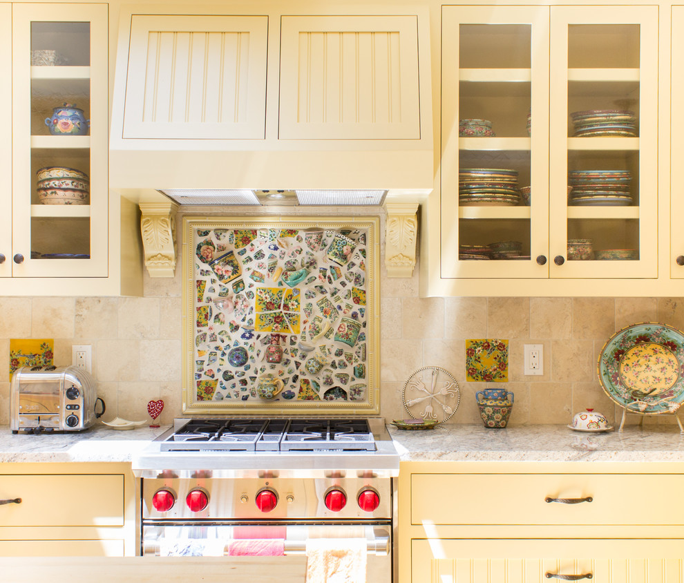 This is an example of a medium sized shabby-chic style l-shaped open plan kitchen in Other with a submerged sink, recessed-panel cabinets, yellow cabinets, beige splashback, mosaic tiled splashback, stainless steel appliances, light hardwood flooring and an island.