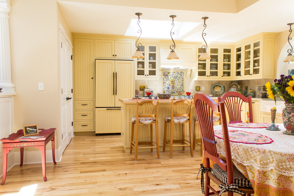 Esempio di una cucina stile shabby di medie dimensioni con lavello sottopiano, ante con riquadro incassato, ante gialle, paraspruzzi beige, paraspruzzi in gres porcellanato e parquet chiaro