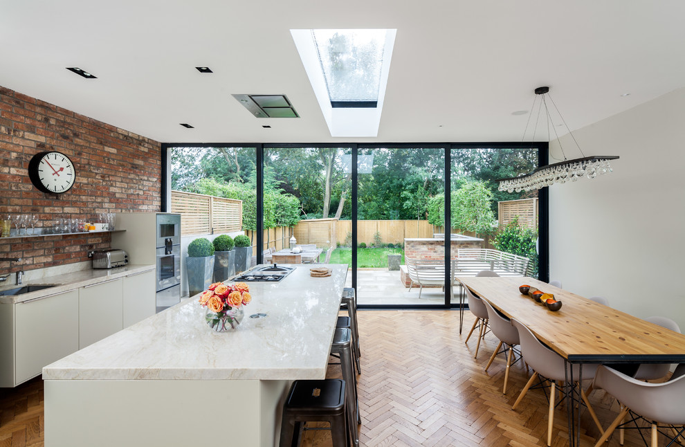 Moderne Wohnküche mit Unterbauwaschbecken, flächenbündigen Schrankfronten, weißen Schränken, Marmor-Arbeitsplatte, Küchenrückwand in Rot, hellem Holzboden und Kücheninsel in London