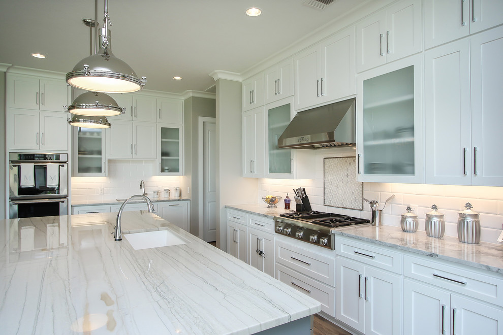 Transitional l-shaped ceramic tile open concept kitchen photo in Houston with an undermount sink, shaker cabinets, white cabinets, quartzite countertops, white backsplash, subway tile backsplash, stainless steel appliances, an island and gray countertops