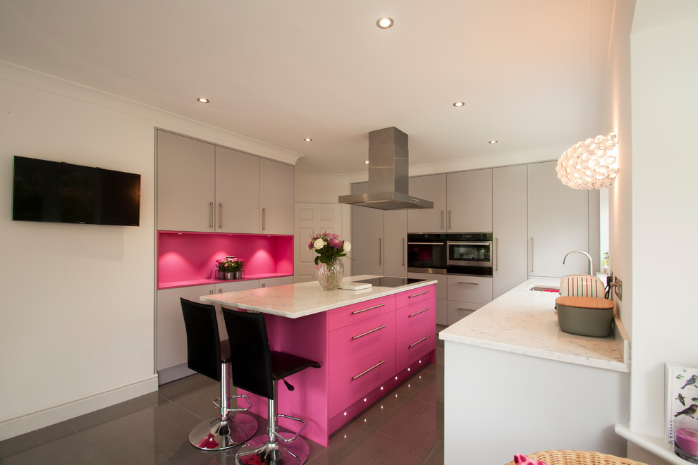Large trendy u-shaped ceramic tile and gray floor kitchen photo in Surrey with flat-panel cabinets, gray cabinets, solid surface countertops, an island, an undermount sink, pink backsplash, black appliances and white countertops