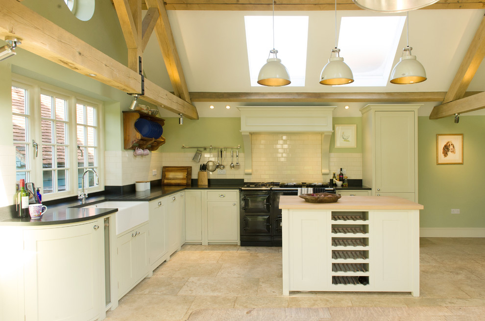 Design ideas for a rural l-shaped kitchen in Berkshire with a belfast sink, shaker cabinets, white cabinets, white splashback, metro tiled splashback, black appliances and travertine flooring.