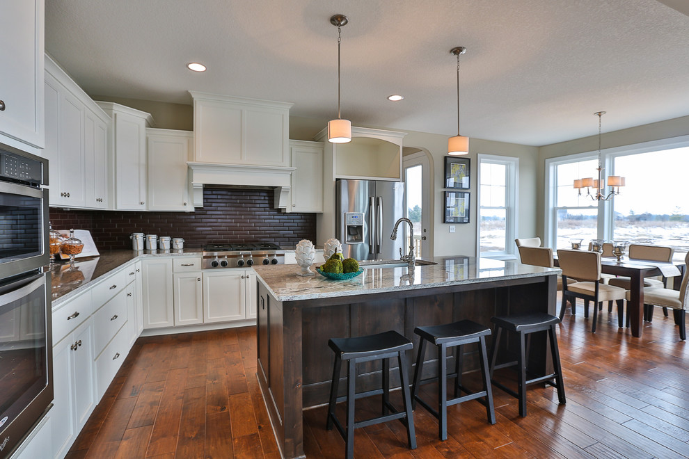 Example of a mid-sized minimalist l-shaped medium tone wood floor eat-in kitchen design in Minneapolis with an undermount sink, recessed-panel cabinets, white cabinets, brown backsplash, glass tile backsplash, stainless steel appliances and an island