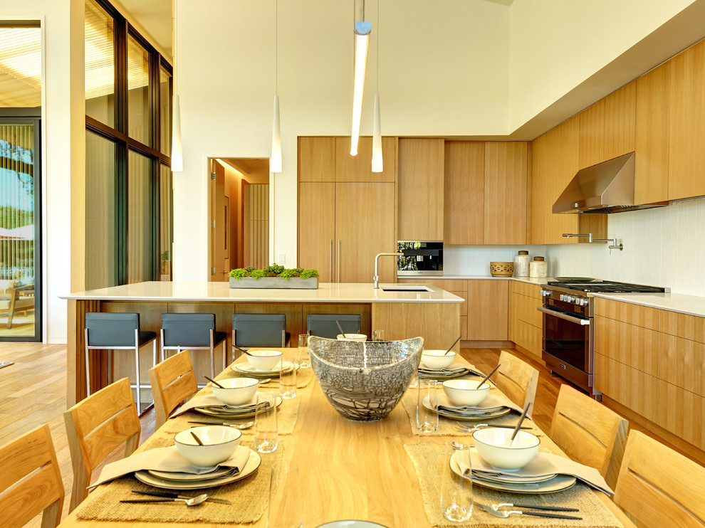 На фото: угловая кухня в современном стиле с обеденным столом, врезной мойкой, плоскими фасадами, коричневыми фасадами, белым фартуком, техникой из нержавеющей стали, полуостровом и коричневым полом с