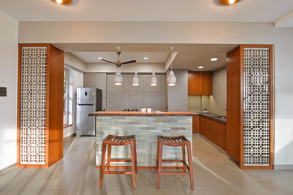Small world-inspired l-shaped open plan kitchen in Mumbai with a submerged sink, flat-panel cabinets, medium wood cabinets, beige splashback, stainless steel appliances, an island and beige floors.