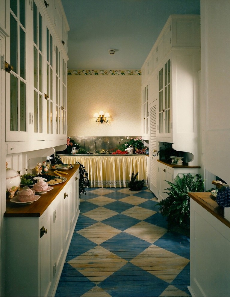 Lantlig inredning av ett kök, med luckor med glaspanel, vita skåp, träbänkskiva, färgglada vitvaror, målat trägolv och blått golv