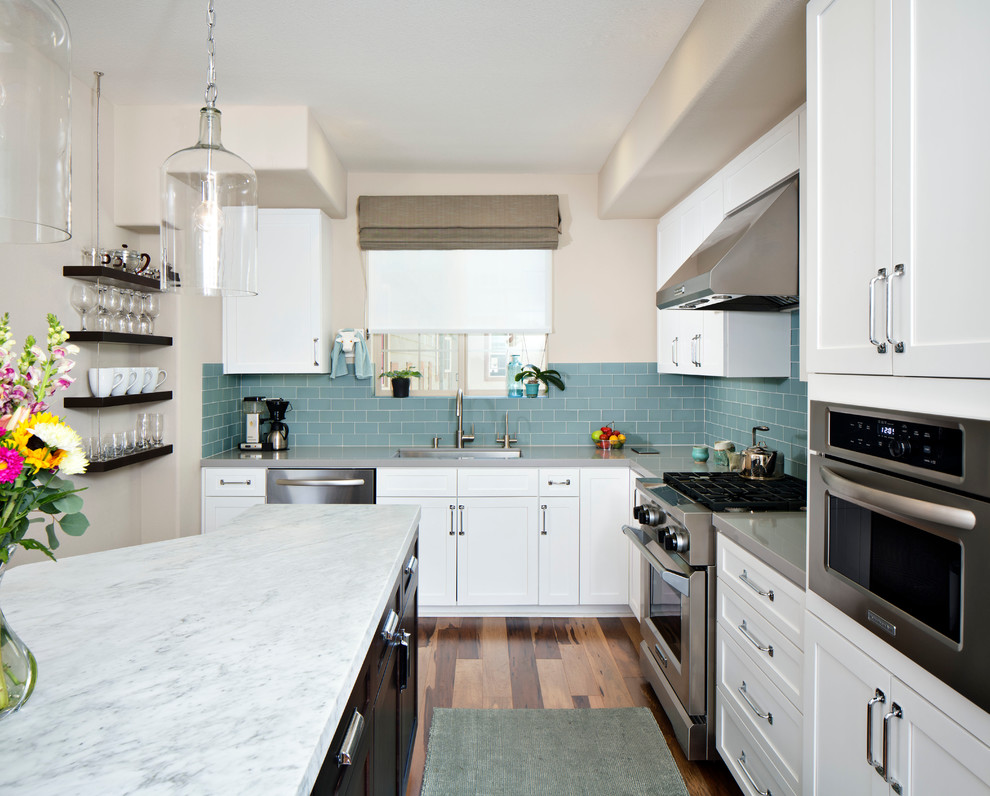 Foto på ett mellanstort funkis kök, med en undermonterad diskho, skåp i shakerstil, vita skåp, bänkskiva i kvarts, blått stänkskydd, stänkskydd i tunnelbanekakel, rostfria vitvaror, mellanmörkt trägolv och en köksö