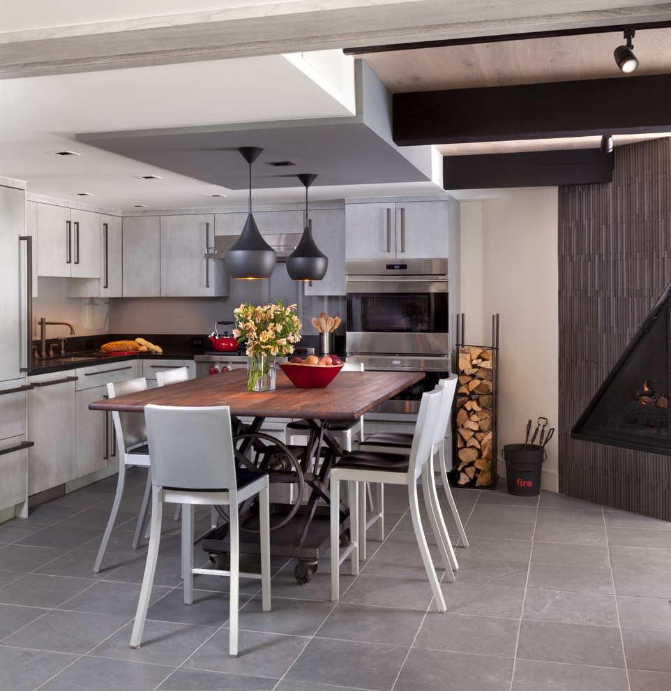 Foto på ett litet 50 tals kök, med en enkel diskho, släta luckor, grå skåp, granitbänkskiva, grått stänkskydd, glaspanel som stänkskydd, integrerade vitvaror, skiffergolv och en köksö