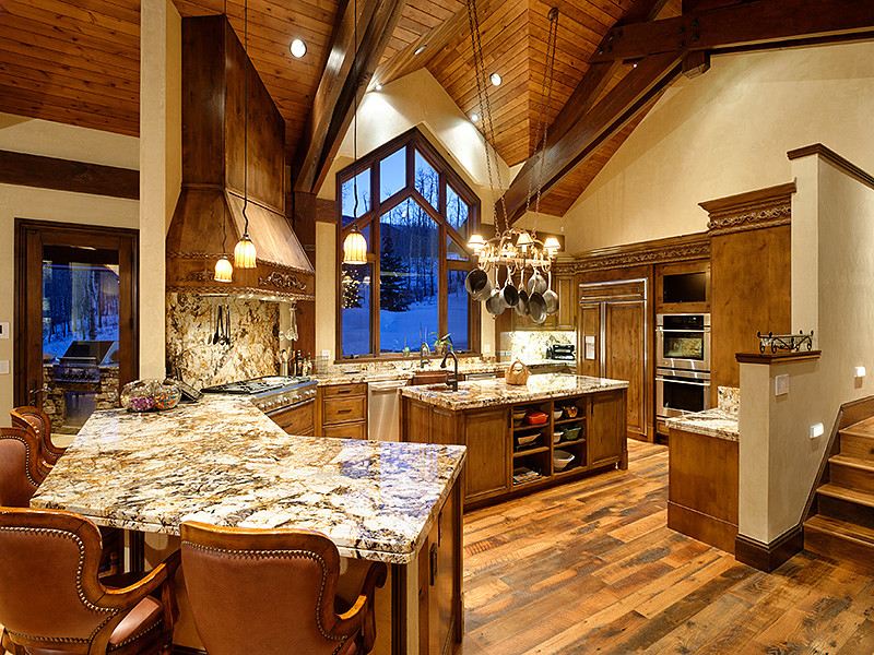 Eat-in kitchen - large rustic u-shaped medium tone wood floor eat-in kitchen idea in Denver with distressed cabinets, an island, a farmhouse sink, recessed-panel cabinets, granite countertops, multicolored backsplash, stone slab backsplash and paneled appliances