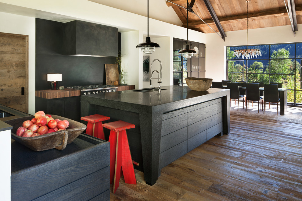 Example of a mountain style galley dark wood floor and brown floor open concept kitchen design in Other with an undermount sink, flat-panel cabinets, black cabinets, black backsplash, an island and black countertops