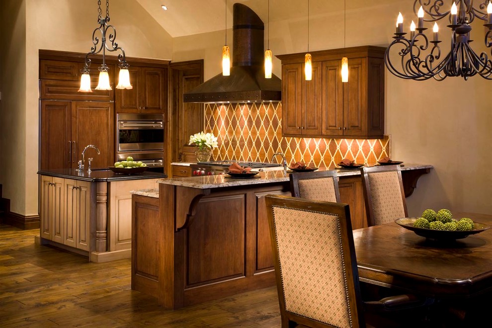 Exemple d'une cuisine américaine chic en bois foncé avec un placard avec porte à panneau surélevé, un plan de travail en granite, une crédence multicolore, un électroménager en acier inoxydable, un sol en bois brun et îlot.
