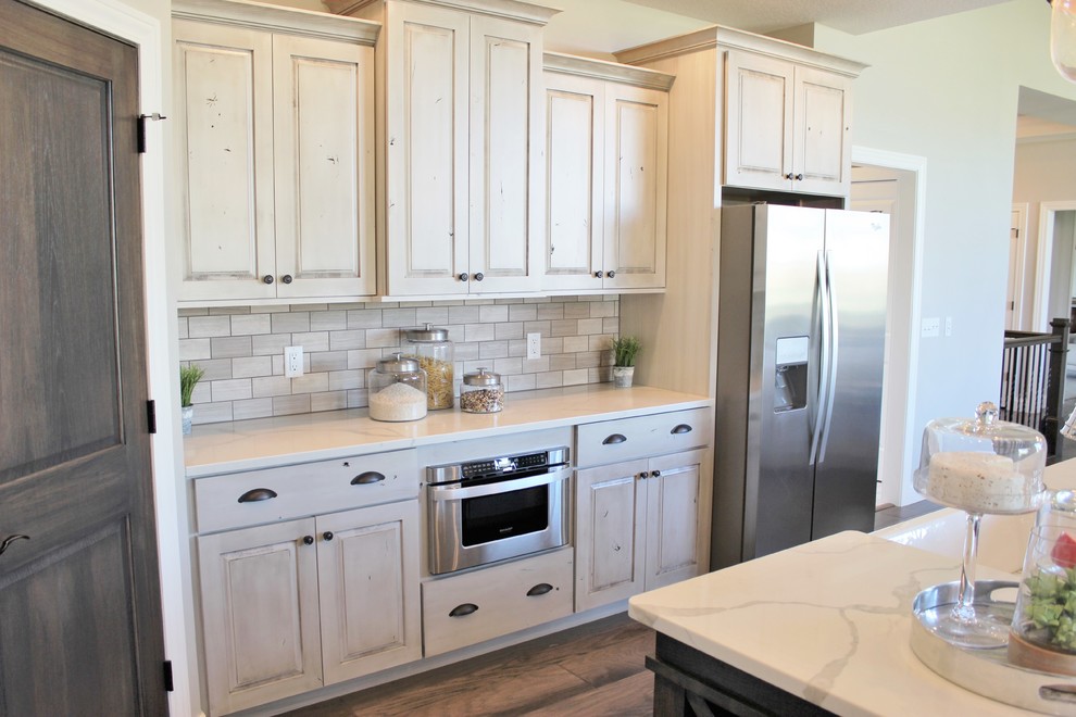Exempel på ett lantligt kök, med en rustik diskho, luckor med upphöjd panel, skåp i slitet trä, bänkskiva i kvarts, grått stänkskydd, stänkskydd i stenkakel, rostfria vitvaror, mellanmörkt trägolv, en köksö och grått golv