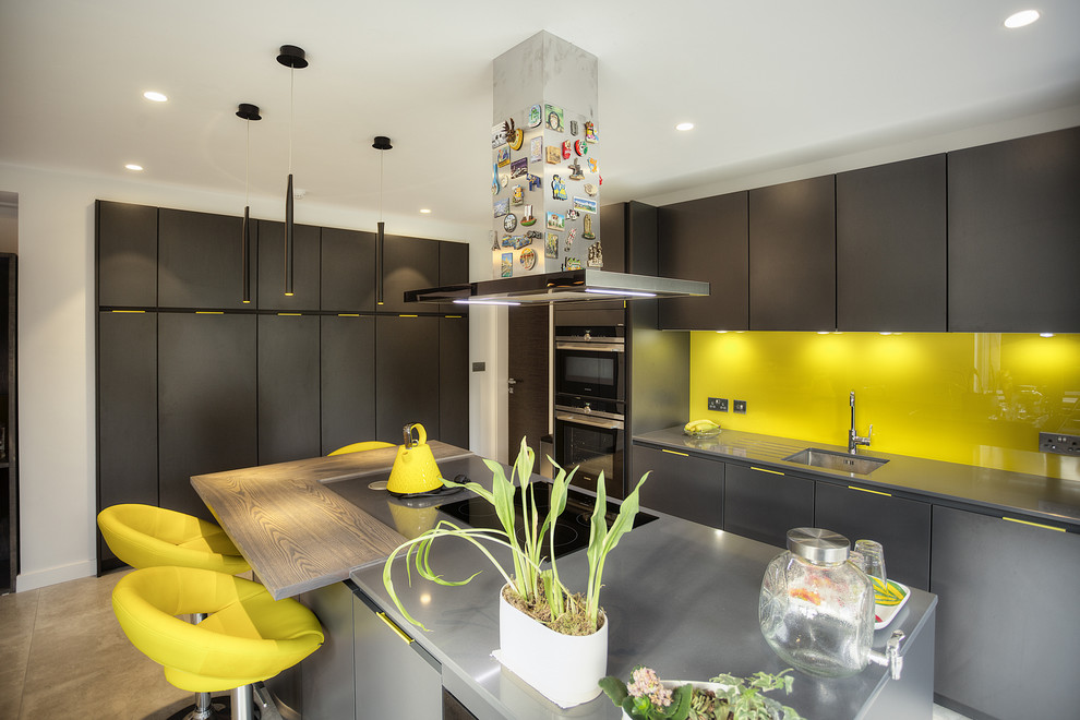 Exempel på ett stort modernt kök, med en undermonterad diskho, släta luckor, grå skåp, bänkskiva i rostfritt stål, gult stänkskydd, glaspanel som stänkskydd, rostfria vitvaror, ljust trägolv och en halv köksö