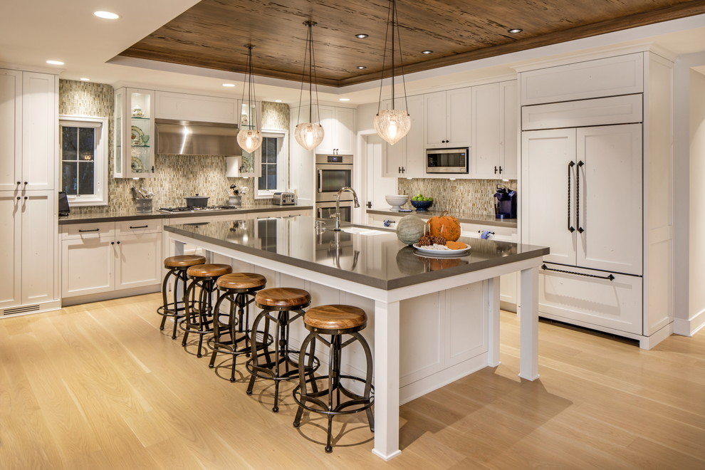 Bild på ett lantligt grå grått kök, med en undermonterad diskho, skåp i shakerstil, vita skåp, flerfärgad stänkskydd, integrerade vitvaror, ljust trägolv, en köksö och beiget golv