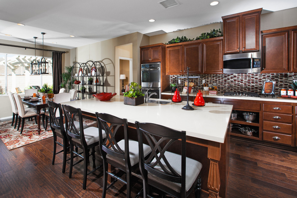 Klassisk inredning av ett mellanstort kök och matrum, med en undermonterad diskho, luckor med infälld panel, bruna skåp, granitbänkskiva, flerfärgad stänkskydd, rostfria vitvaror och en köksö