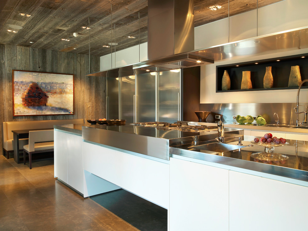 Foto på ett mellanstort funkis kök, med en integrerad diskho, stänkskydd i metallkakel, släta luckor, bänkskiva i rostfritt stål, rostfria vitvaror, betonggolv, en köksö och brunt golv