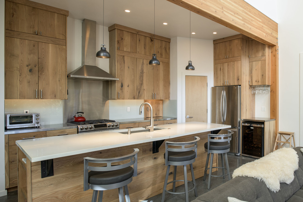 Exempel på ett rustikt vit vitt kök med öppen planlösning, med en undermonterad diskho, släta luckor, skåp i ljust trä, stänkskydd med metallisk yta, rostfria vitvaror, betonggolv, en köksö och grått golv