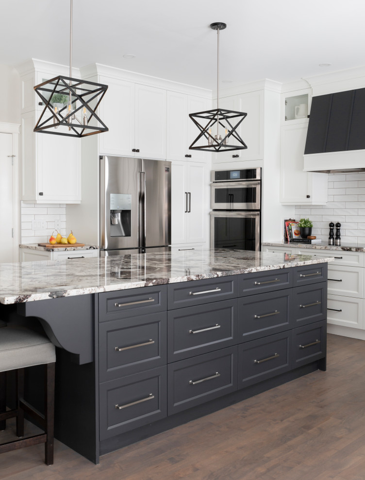Klassisk inredning av ett stort grå grått kök, med en undermonterad diskho, skåp i shakerstil, vita skåp, granitbänkskiva, vitt stänkskydd, stänkskydd i tunnelbanekakel, rostfria vitvaror, mellanmörkt trägolv, en köksö och grått golv