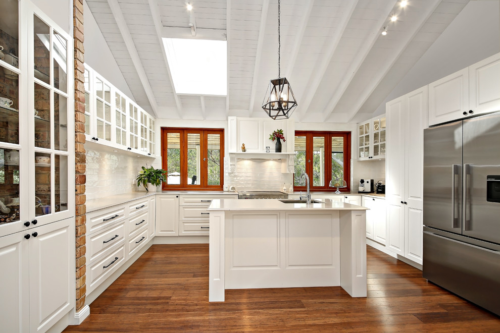 Exempel på ett mellanstort klassiskt u-kök, med en nedsänkt diskho, luckor med upphöjd panel, vita skåp, vitt stänkskydd, rostfria vitvaror, mellanmörkt trägolv, flera köksöar och brunt golv