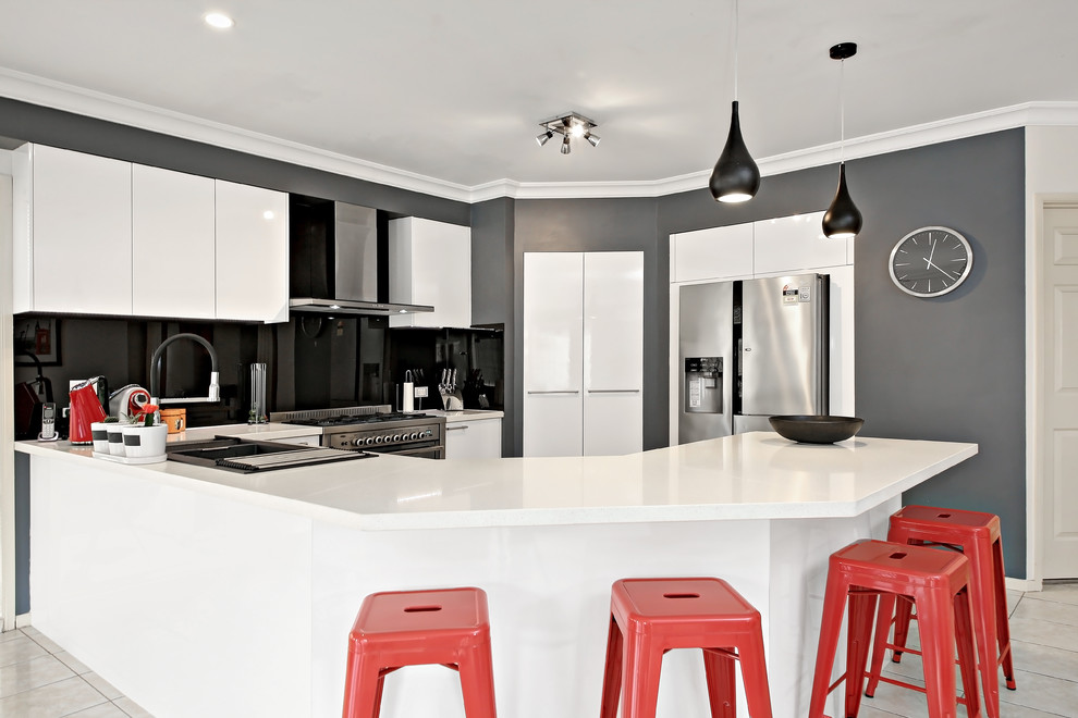 Foto på ett mellanstort funkis vit u-kök, med en dubbel diskho, släta luckor, bänkskiva i kvarts, svart stänkskydd, spegel som stänkskydd, rostfria vitvaror, flera köksöar och beiget golv