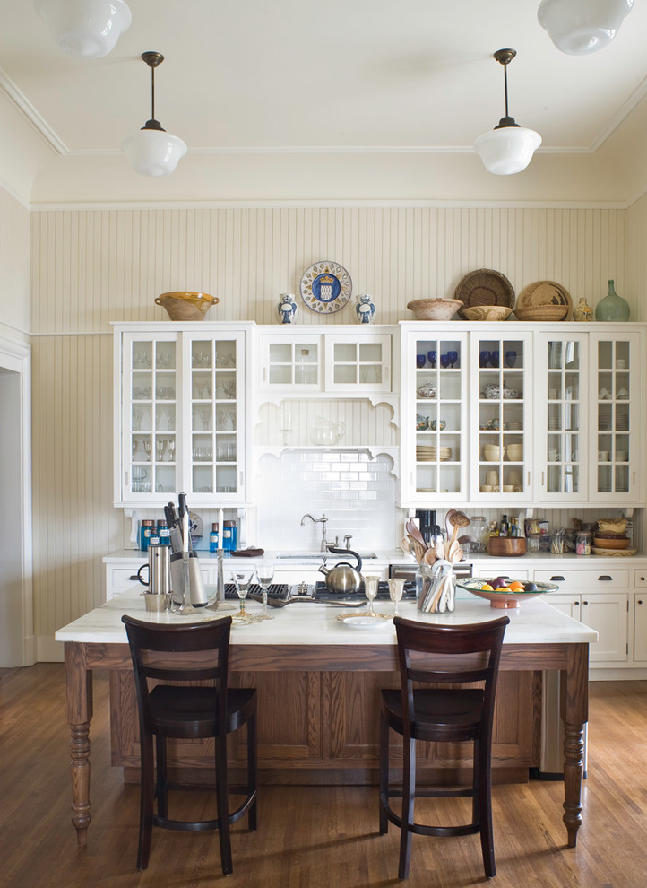 Inspiration for a victorian galley kitchen in New York with glass-front cabinets, white cabinets, white splashback, metro tiled splashback, dark hardwood flooring and an island.