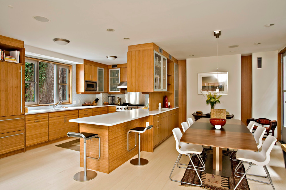 Moderne Wohnküche in U-Form mit flächenbündigen Schrankfronten, hellbraunen Holzschränken, Küchenrückwand in Weiß, Rückwand aus Metrofliesen und Elektrogeräten mit Frontblende in New York