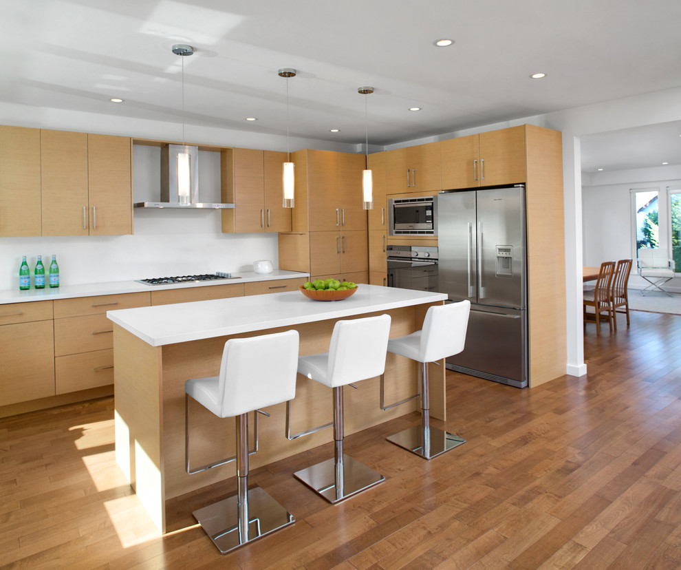 Example of a mid-sized trendy l-shaped medium tone wood floor open concept kitchen design in Vancouver with an undermount sink, flat-panel cabinets, light wood cabinets, solid surface countertops, stainless steel appliances and an island